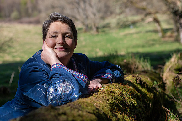 Picture shows storyteller Lindsey Gibb leaning over a log in a springtime woodland near Dunkeld, Perthshire (Scotland).