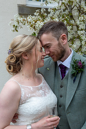 Bride and groom hold looking lovingly in each other's eyes in front of beautiful white cherry blossom.