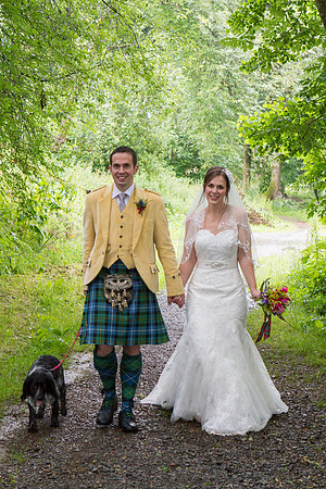 Bridge and groom walking in the rain on a path alongside the River Tay in Aberfeldy, together with their dog.