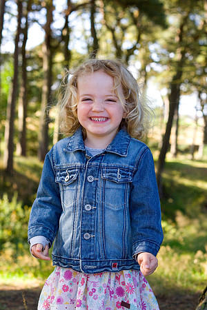 Portrait of a girl smiling into the camera in a sunny woodland in Perthshire, Scotland.