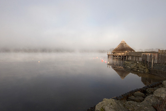 A reconstructed roundhouse (crannog) looms out of the mist on Loch Tay near Kenmore, Perthshire, Scotland.