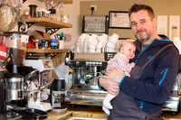 A father holds his baby daughter while standing behind the counter of his coffeeshop "Habitat" in Aberfeldy, Perthshire (Scotland).