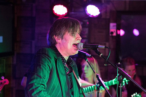 Singer Justin Currie from Del Amitri on stage holding his guitar and singing, together with his band mates from Los Supremos at the Bandstand Beer and Music Festival in Nairn, Scotland.