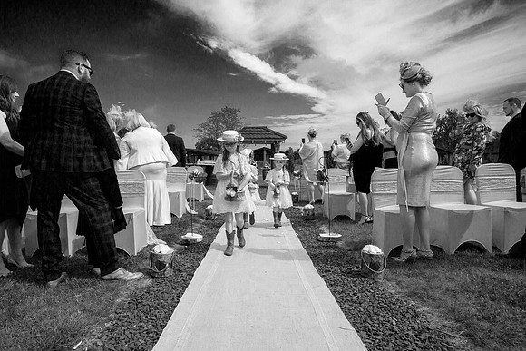 A black and white photo of flower girls walking down the isle on a sunny day at the Silverwood Lodges near Errol.