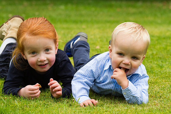 Two toddler siblings posing for a family photo, lying down on the grass at a private home in Perthshire, Scotland.