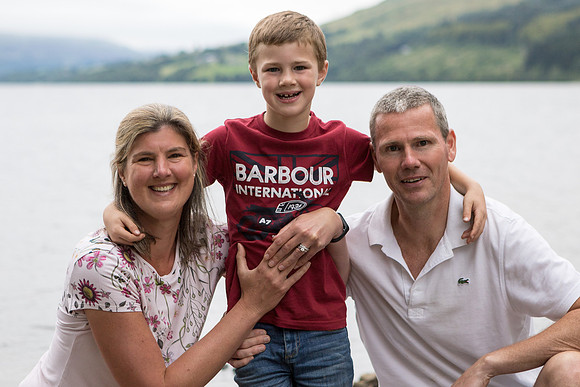 A family of three poses together for a family photo in front of Loch Tay, Fearnan, Perthshire (Scotland).